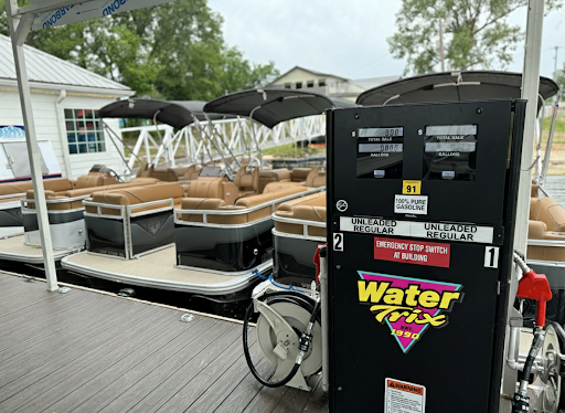 Gas pump on dock with pontoon boats and building in background.